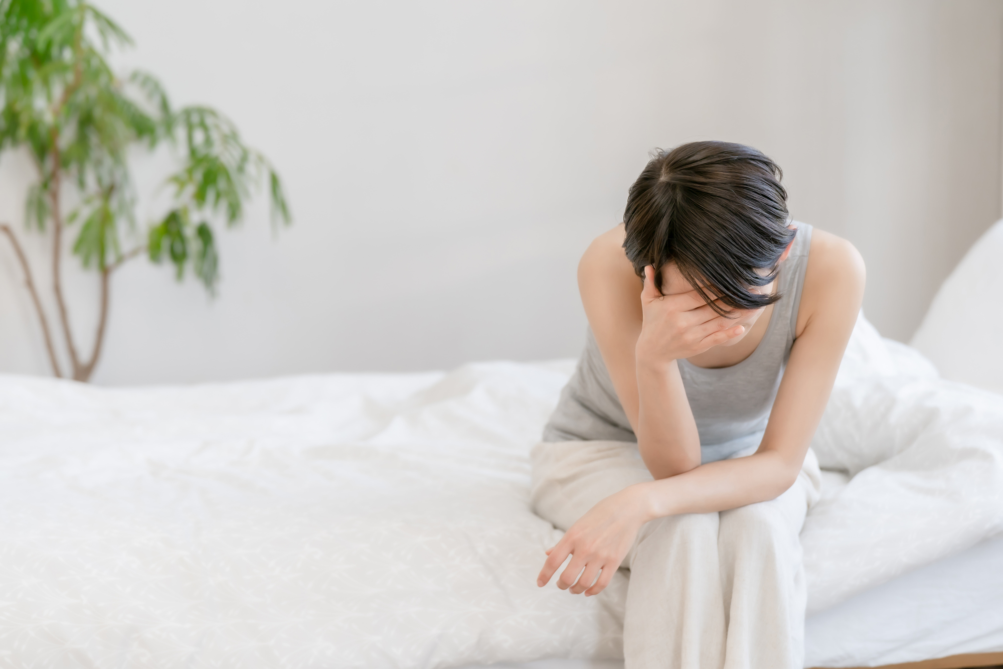 ベッドの端で頭を抱える女性